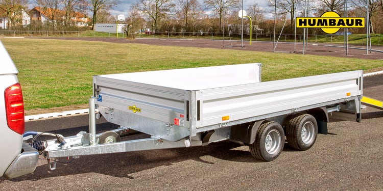 Humbaur Tandemanhänger an Pick-up auf asphaltiertem Platz mit Rasenfläche