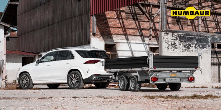 Humbaur Kipperanhänger an weißem SUV vor einem Industriegebäude