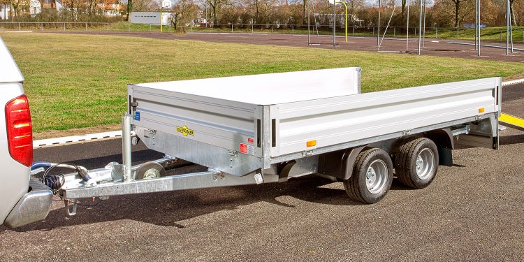 Humbaur Tandemanhänger an Pick-up auf asphaltiertem Platz mit Rasenfläche