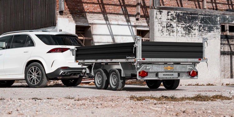 Humbaur Kipperanhänger an weißem SUV vor einem Industriegebäude