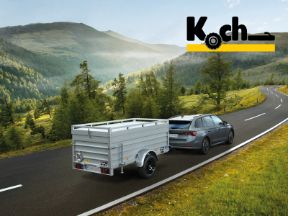 Ein Anhänger von Koch wird von einem Fahrzeug in einer Berglandschaft gezogen.