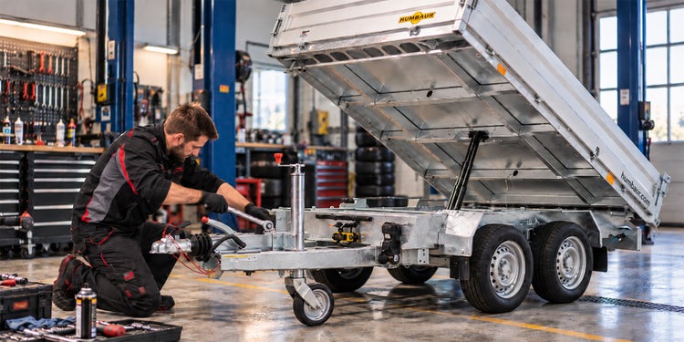 KI-generiertes Foto eines Mechanikers, der einen Humbaur Anhänger in der Werkstatt wartet.